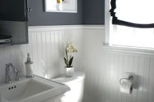 a contrasting bathroom with black walls, white paneling, a pedestal sink, a mirror cabinet and a black and white shade on the window
