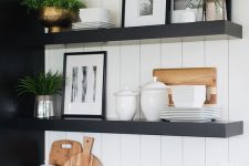 a contrasting kitchen with black cabinets, white countertops and a backsplash, thick black shelves and potted plants