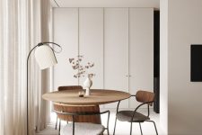 a cool Japandi space done in neutrals, with a round table and cool chairs, a floor lamp and a large sleek storage unit