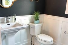 a cool contrasting bathroom with hex tiles, white paneling and black walls, a pedestal sink, a catchily shaped mirror, wall decor and sconces