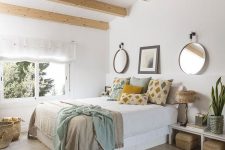 a cozy and bright bedroom with wooden beams, a white bed with storage, low nightstands, bright printed pillows and baskets