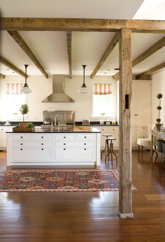 a cozy rustic chic kitchen with neutral cabinets, black countertops, wooden beams and pendant lamps plus bright textiles