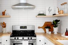 a cute white kitchen with black fixtures, light-stained butcherblock countertops and floating shelves plus a skinny tile backsplash