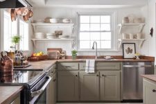 a farmhouse kitchen with olive green cabinetry, butcherblock countertops, wooden beams that echo with them and open shelving
