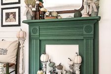 a faux fireplace with a green mantel, an arrangement of pumpkins on tall stands, eucalyptus, wheat and pumpkins on the mantel