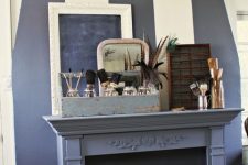 a faux fireplace with a refined mantel, bottles, brushes, vases and whitewashed stacked suitcases inside the fireplace