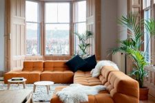 a light-filled living room with gorgeous views of the city, an orange sectional, round coffee tables and dark pillows
