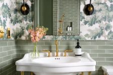 a little and pretty powder room with floral print wallpaper, green tiles, an arched mirror, a console sink and vintage sconces
