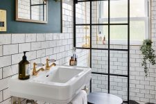 a lovely art deco bathroom with white subway tiles, a console sink, a shower space with a glass wall, brass touches for maximal elegance