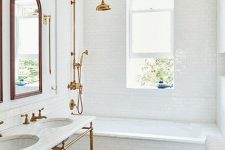 a lovely bathroom with penny tiles on the floor, a tub clad with white subway tiles, a double console sink, arched mirrors and brass and copper touches