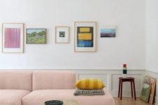 a lovely bright living room with a pink low sofa, a colorful gallery wall, panelling, a round table and a creamy rug is cool