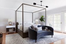 a lovely modern bedroom with a canopy bed, a grey curved sofa, matching nightstands, table lamps and a chic chandelier