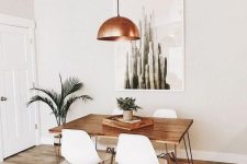 a mid-century modern dining space with a hairpin leg table, white chairs, a copper pendant lamp, potted plants and a cool boho rug