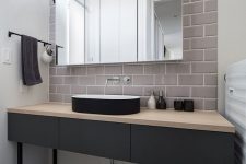 a minimalist bathroom with a matte black vanity, a sleek black vessel sink, a large mirror cabinet and a grey subway tile accent wall