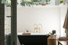 a modern bathroom clad with white subway and penny tiles, a vintage black bathtub, a shower, a bench and a tree stump side table