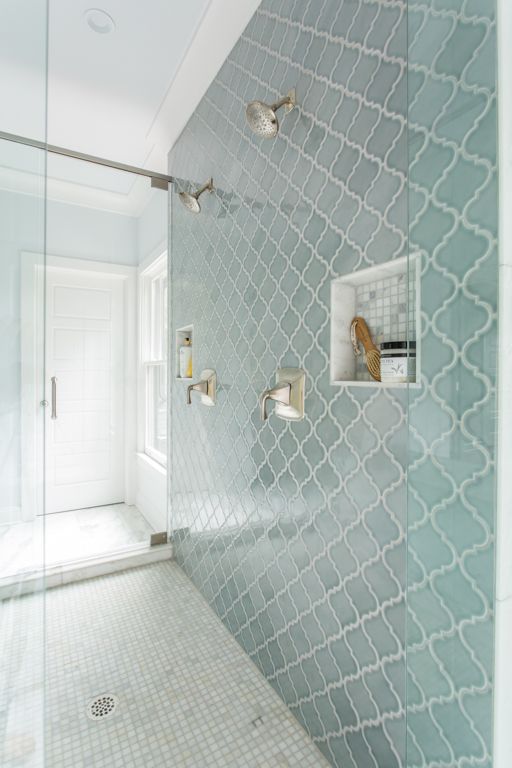 a modern bathroom with neutral tiles on the floor and a blue arabesque tile accent wall with niches for storage is a very stylish and cool idea