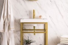a modern bathroom with stone-imitating wallpaper, a chevron wooden floor, a console sink, a round mirror in a gold frame