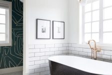 a modern bathroom with two different types of tiles, a sleek black clad tub, a catchy pendant lamp and pritned wallpaper