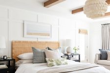 a modern coastal bedroom with stained wooden beams, a bed with a rattan headboard, neutral bedding, black nightstands, neutral bedding