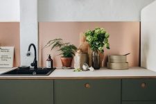 a modern dark green kitchen with white countertops, a copper backsplash and black fixtures is a stylish idea and the colors look great with each other