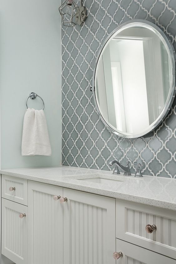 a modern farmhouse bathroom with grey arabesque tiles for an accent, white planked vanities, a round mirror and a simple towel