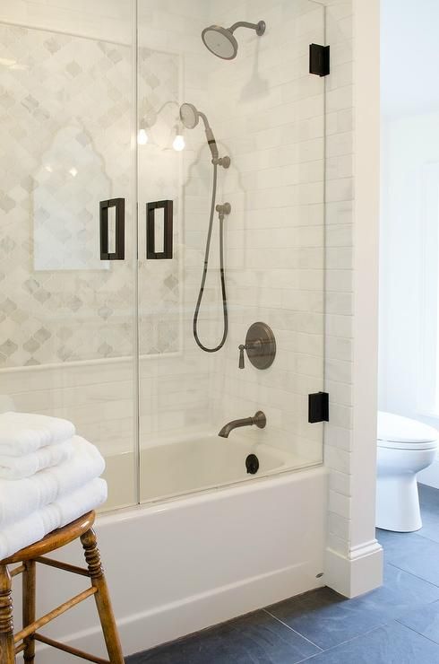 a modern farmhouse bathroom with grye tiles on the floor, white subway and marble arabesque tiles in the bathing space and a wooden stool
