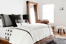 a modern farmhouse bedroom with light-stained wooden beams, a rich-stained wooden bed, black and white bedding and layered rugs