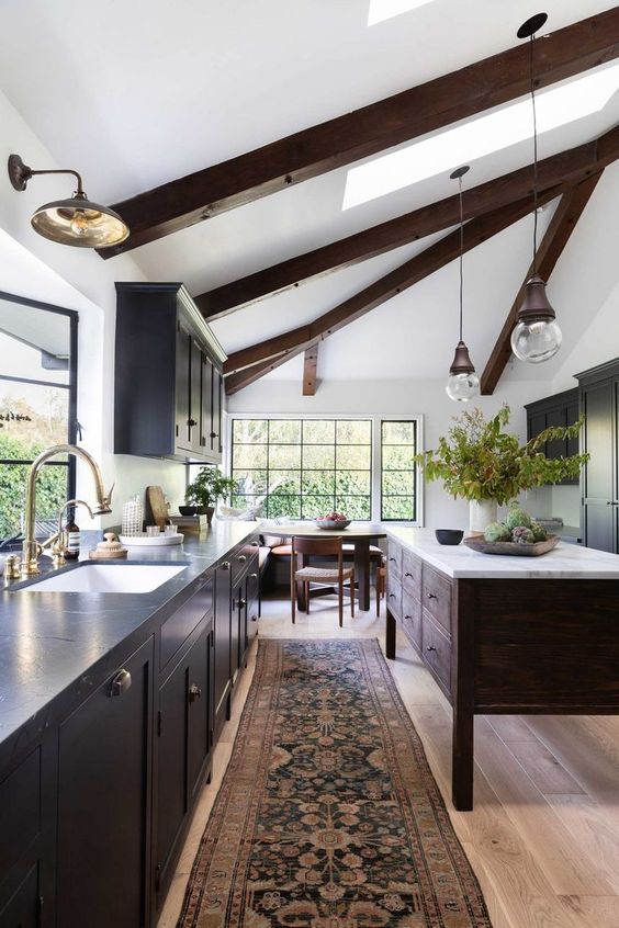 a modern farmhouse kitchen with navy cabinets, a dark stained kitchen island, dark stained beams and vintage lamps