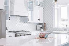a modern white kitchen with black handles, a large white hood, a white arabesque tile backsplash and a wall is elegant