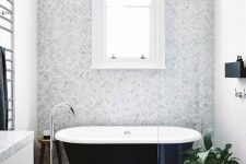 a neutral and chic bathroom with a grey marble accent wall, dark tiles on the floor, a black clawfoot tub, a white vanity and a black mini shelf