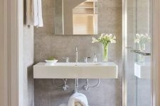 a neutral bathroom with a floating sink, a stand with towels, a mirror with no frame and a shower space enclosed in glass