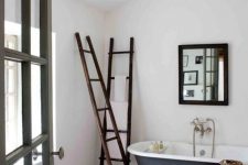 a neutral bathroom with wodoen beams, a blue clawfoot tub, a bench, dark stained ladders and a black chair plus a mirror