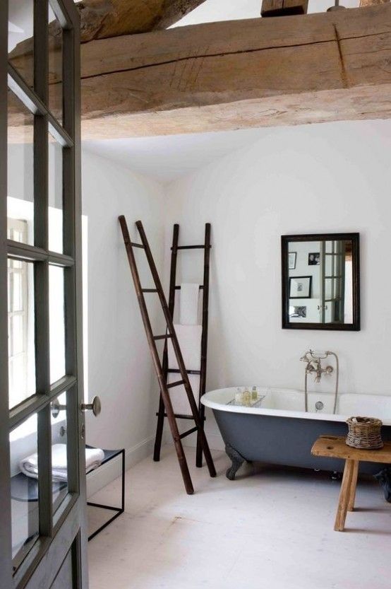 a neutral bathroom with wodoen beams, a blue clawfoot tub, a bench, dark stained ladders and a black chair plus a mirror