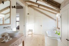 a neutral bathroom with wooden beams and a wooden floor, a light-stained vanity, a clad bathtub and a large wardrobe plus a large mirror