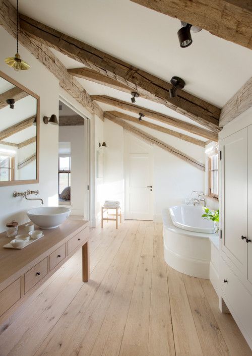 a neutral bathroom with wooden beams and a wooden floor, a light stained vanity, a clad bathtub and a large wardrobe plus a large mirror