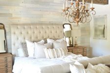 a neutral farmhouse bedroom with a catchy wallpaper accent wall, wooden beams, neutral furniture and stained nightstands plus a refined chandelier
