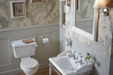 a neutral vintage powder room with floral wallpaper, grey panels, a console sink and a small gallery wall plus a mirror in an ornated frame