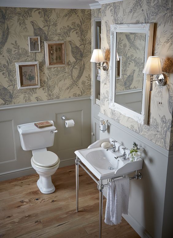 a neutral vintage powder room with floral wallpaper, grey panels, a console sink and a small gallery wall plus a mirror in an ornated frame