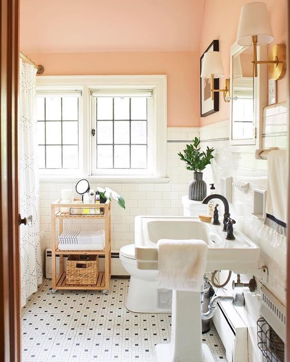 a pretty and welcoming bathroom with peachy walls and a ceiling, white subway tiles and black and white ones, a pedestal sink, a wooden storage unit and black fixtures