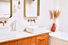 a pretty bright bathroom wiht a terrazzo floor, a light-stained vanity with two sinks, mirrors in gilded frames, a rich-stained wooden beam