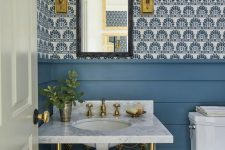 a pretty bright powder room with blue wallpaper and blue planks on the walls, a console sink, elegant sconces and a basket for trash