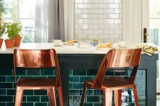 a pretty kitchen with white tiles and a kitchen island clad with emerald tiles, with chic copper stools and pendant lamps is wow