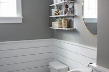 a pretty modern farmhouse bathroom with grey walls and white planks on the walls, a round mirror, a pedestal sink, a small yet practical pendant shelf
