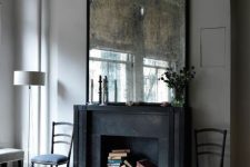 a refined living room with a black fireplace that is sued for book storage and a vintage mirror for a more exquisite look in the space
