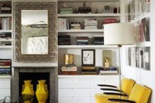 a refined living room with built-in shelves, yellow chairs, a built-in fireplace and yellow vases, a gallery wall and a floor lamp