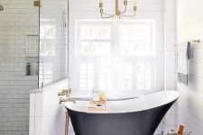 a refined modern bathroom with subway and hex tiles, a planked wall, a black vintage bathtub and a chic gilded chandelier