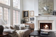 a refined neutral living room with a low grey sofa with lots of pillows, a low coffee table, a fireplace, a crystal chandelier and a gallery wall