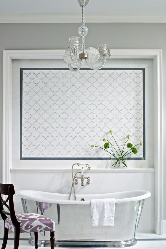 a refined vintage bathroom with grey walls, a white arabesque tile accent, a shiny polished bathtub and a chic crystal chandelier