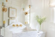 a refined white bathroom with paneled walls, a mirror and a floating stone sink attached to it, some sconces and lamps and white appliances