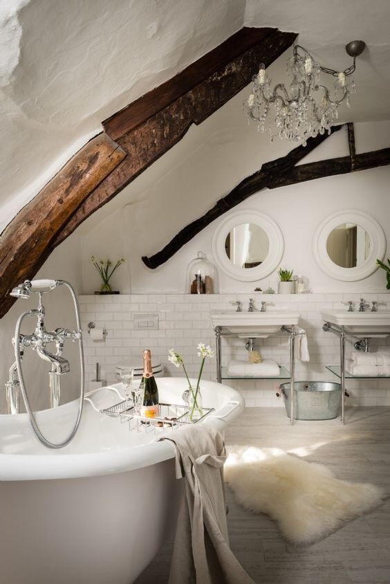 a refined white bathroom with white subway tiles, whitewashed floors, two free standing sinks, round mirrors and dark stained beams